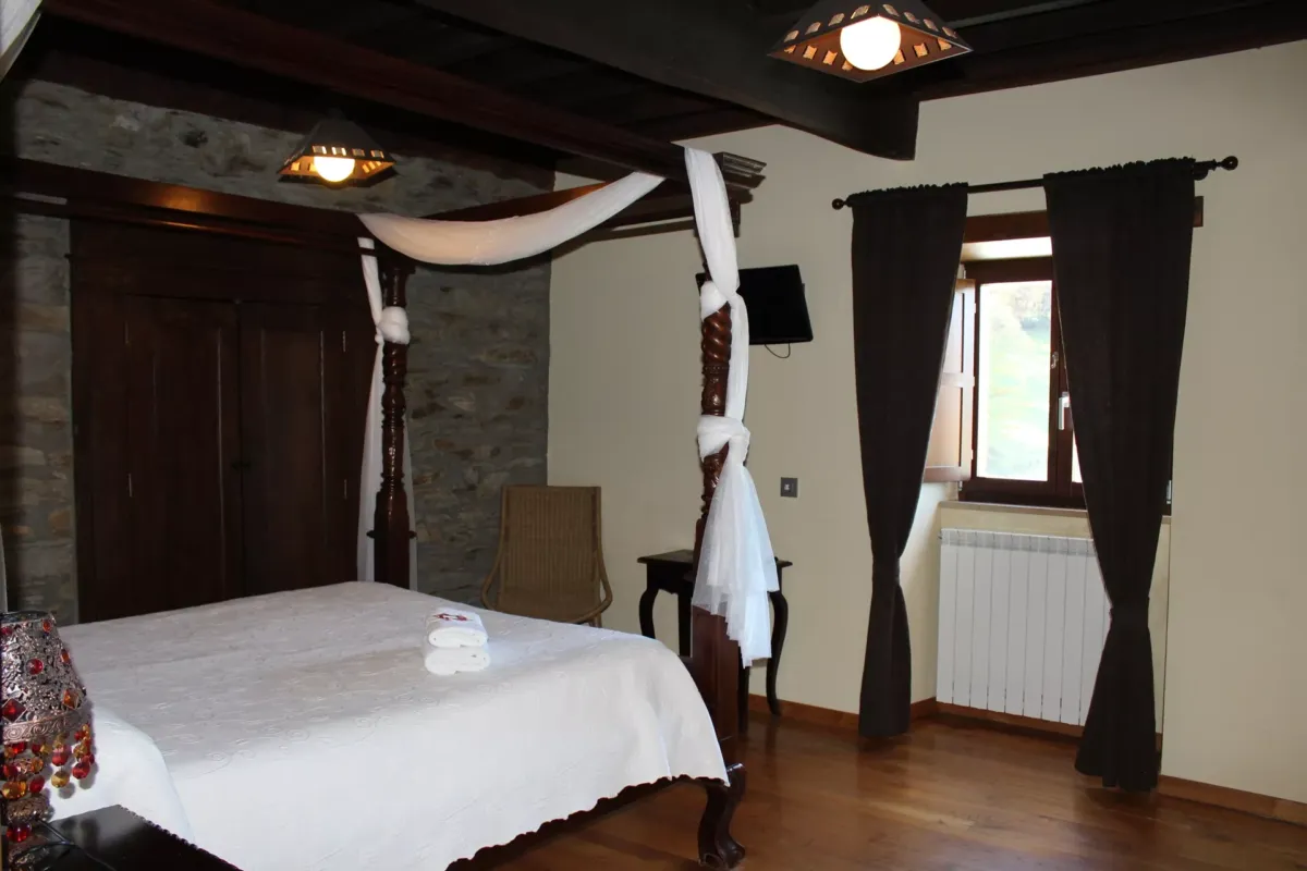 Vista general de la Habitación Afrodita con una cama, armario, silla de mimbre, ventana y radiador